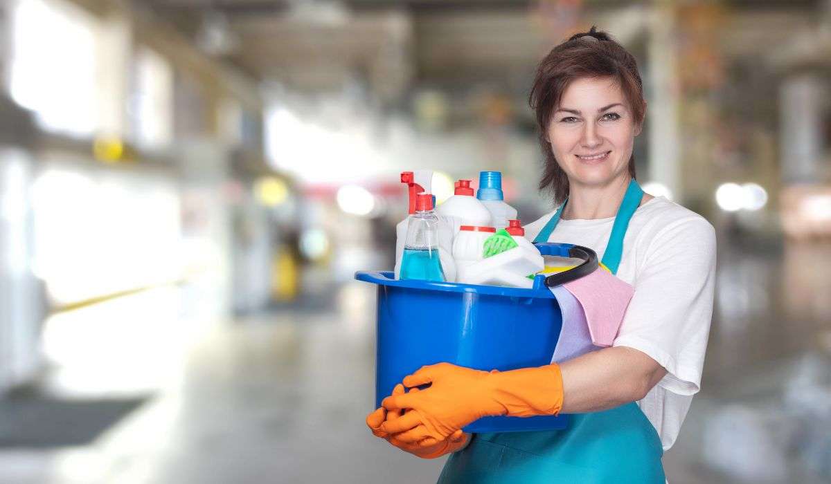 Smiling cleaning lady in Limassol holding a blue bucket filled with professional cleaning products.