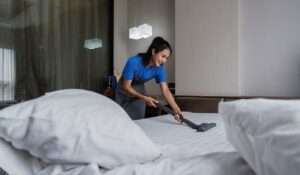 Cleaning lady vacuuming a bed in a modern bedroom as part of residential maid services.